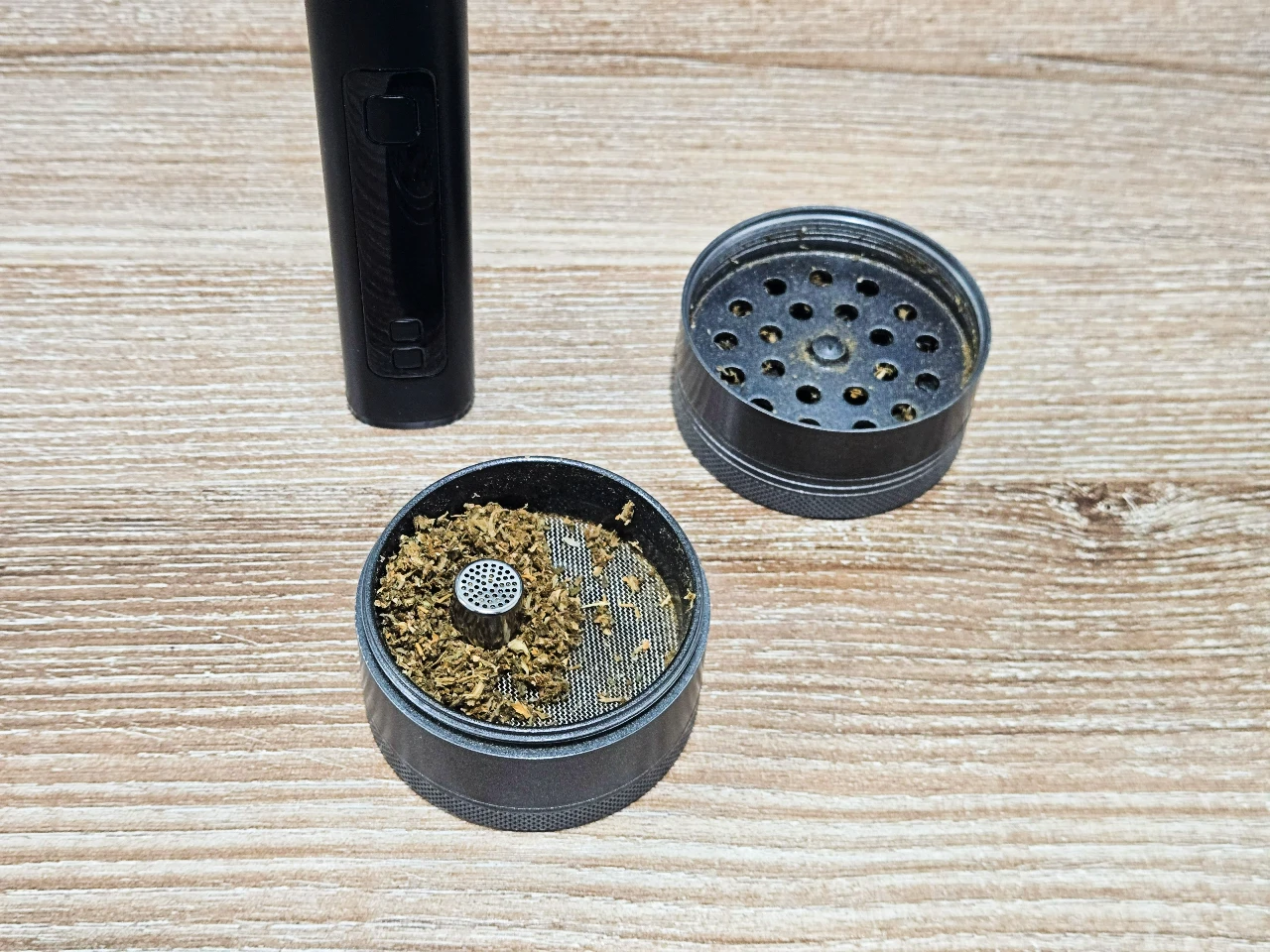 Black XMAX V4 Pro vaporizer next to open herb grinder and metal dosing capsule