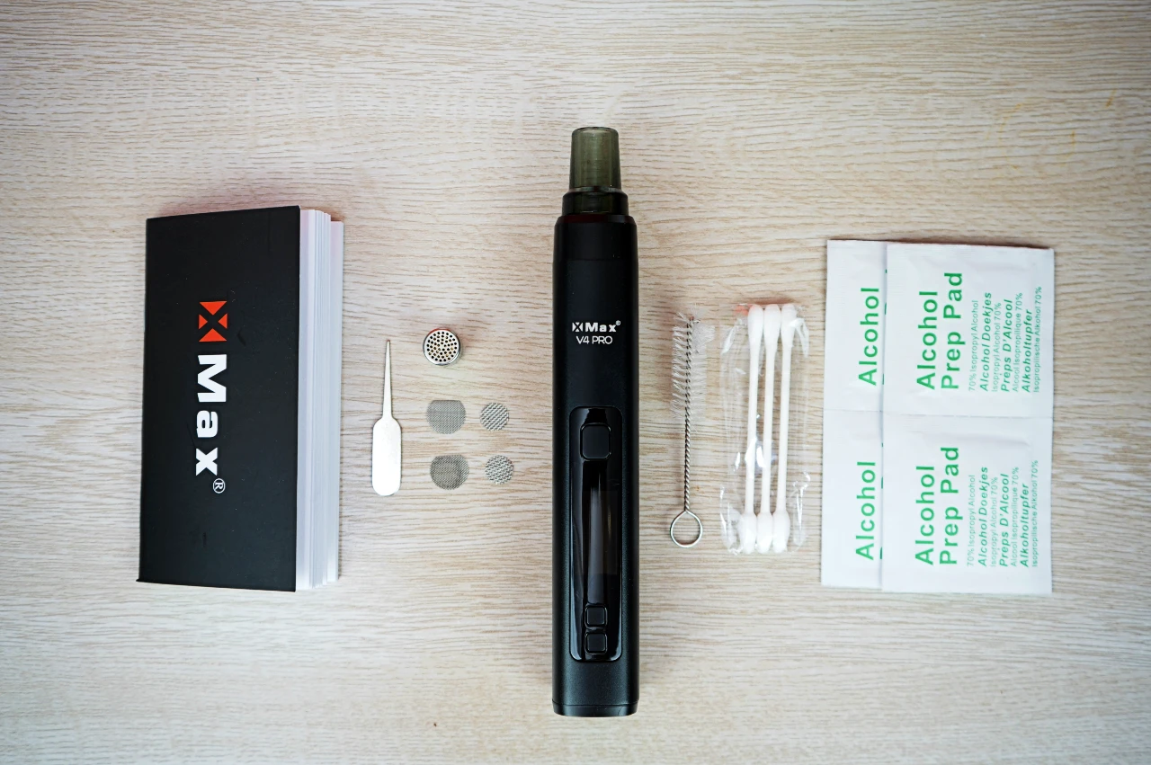 Black XMax V4 Pro dry herb vaporizer kit with user manual, cleaning brush, alcohol prep pads, and accessories.