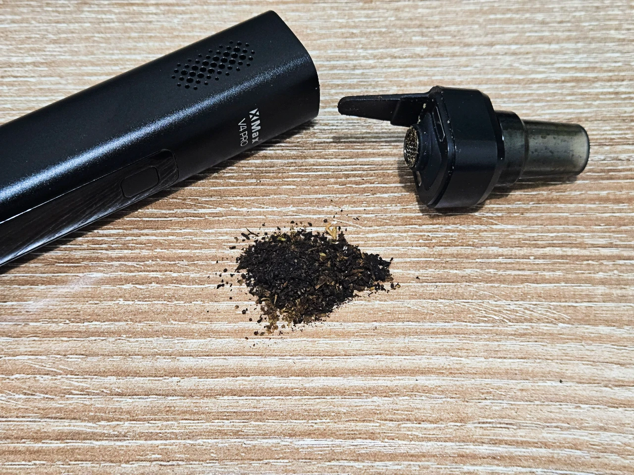 XMAX V4 Pro black dry herb vaporizer body next to detached mouthpiece and vaped herb